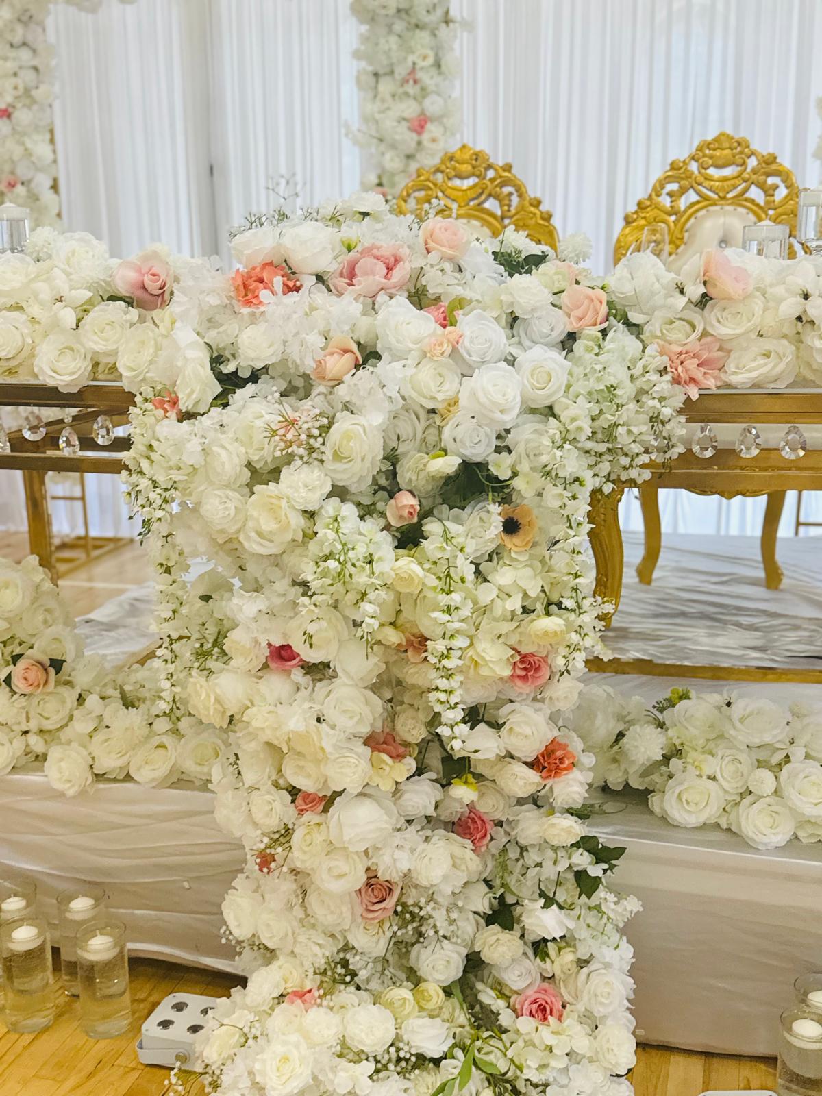 Cascading white and blush floral installation in front of ornate gold chairs