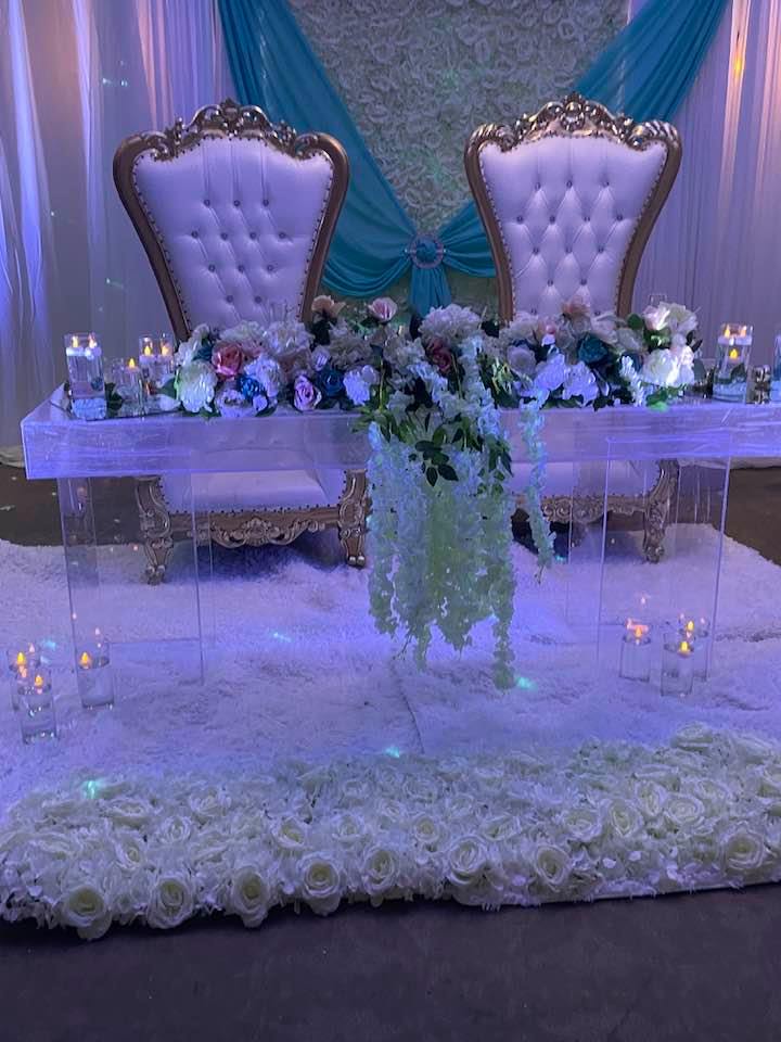 Wedding sweetheart table with gold thrones, teal-and-white draped backdrop, and hanging florals