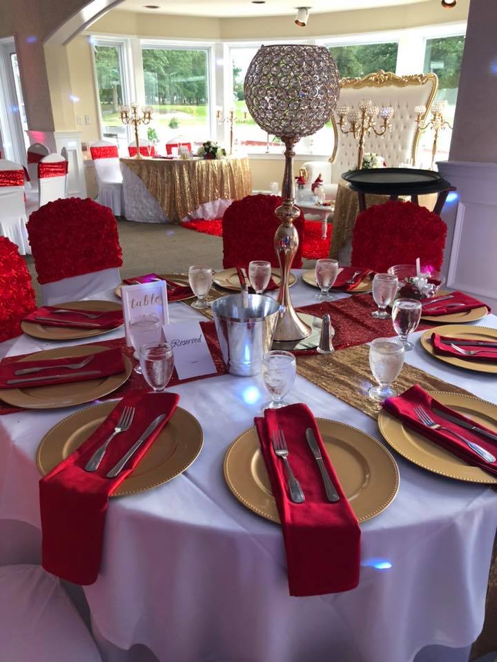 Reception table set with red rose chair covers, gold chargers, red napkins, and crystal candelabra centerpieces
