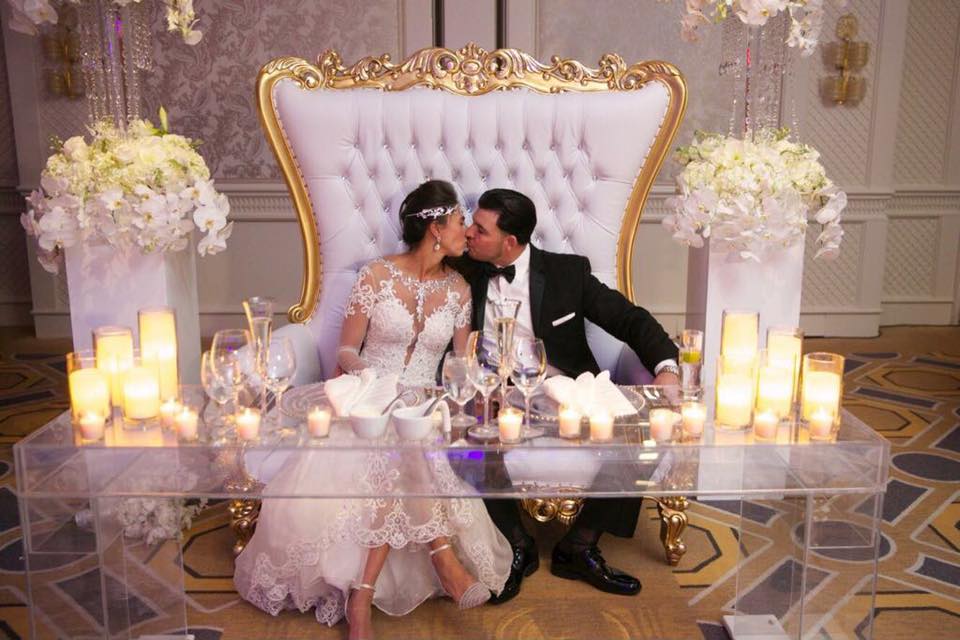 Bride and groom sharing a kiss at a gold-framed sweetheart table surrounded by candles and white florals